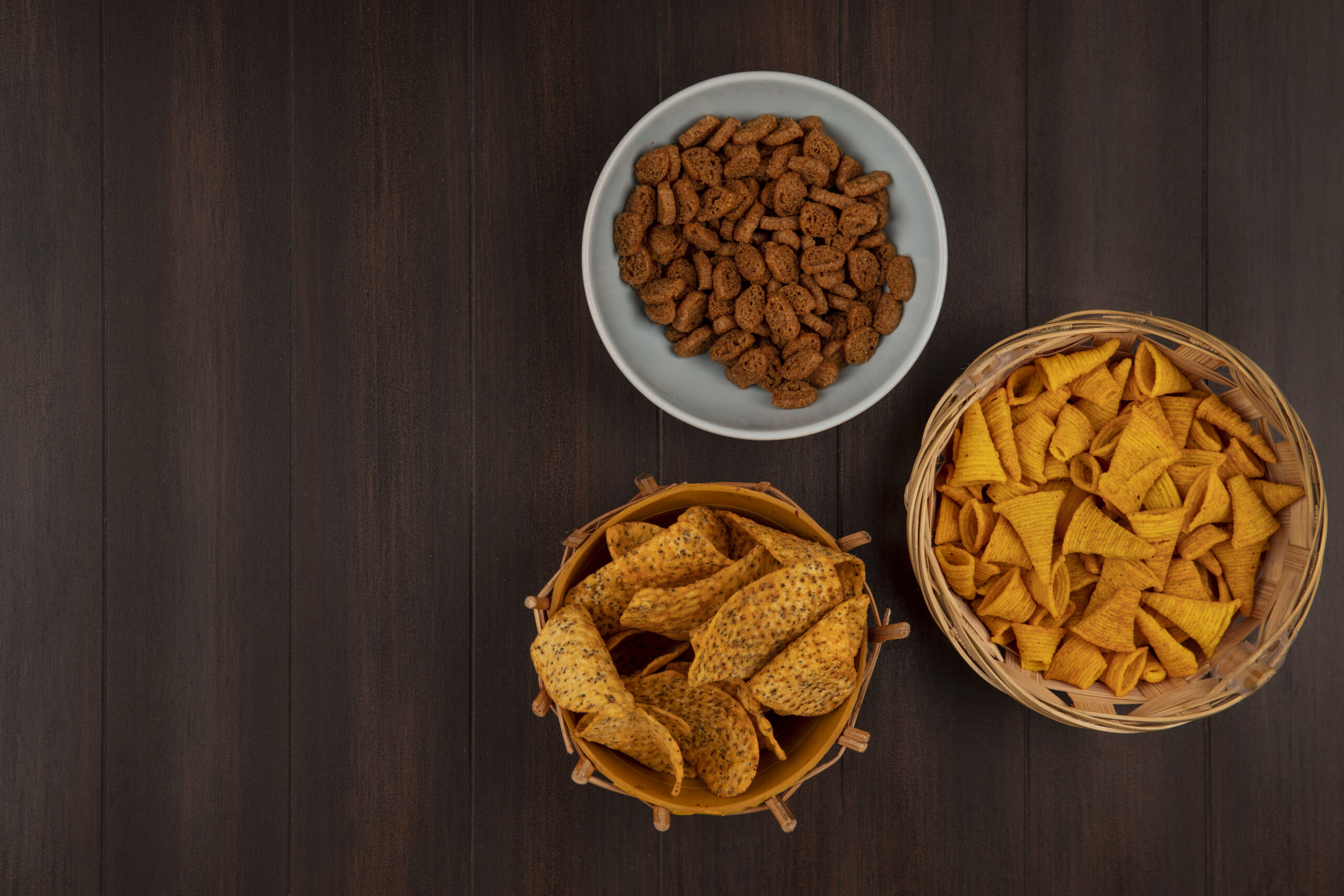 top view of crispy tasty rye rusks on a bowl with spicy chips on a bucket with bugles chips on a bucket on a wooden background with copy space
