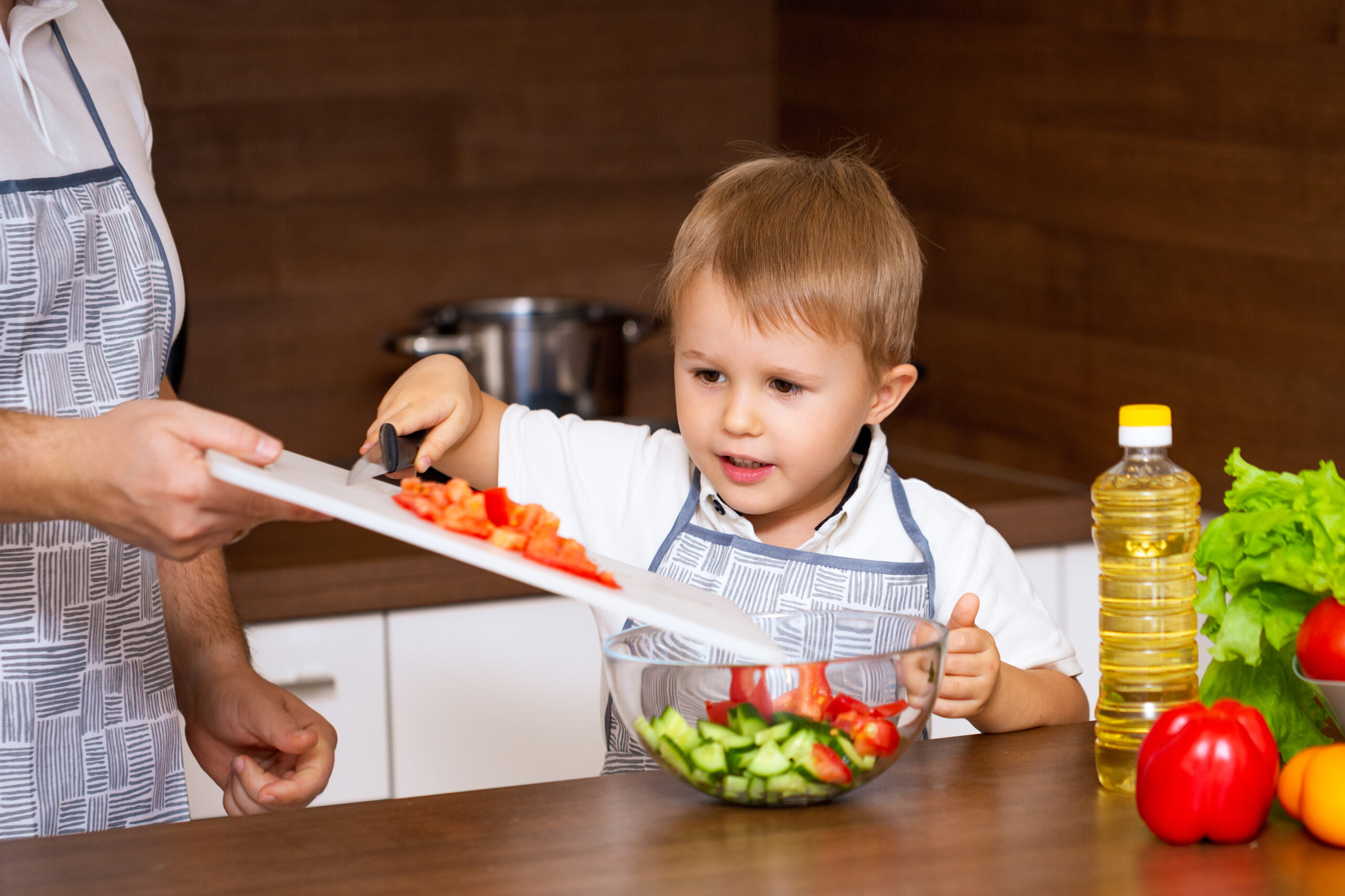 Happy father teaches son to cut salad in the kitchen